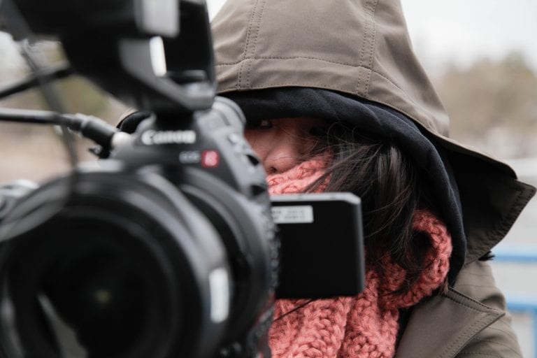 Close up of camera woman's face covered up in order to stay warm with a camera in front of her face.