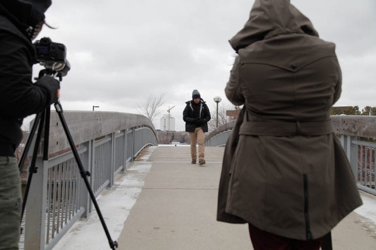 The backs of 2 camera women with Nan Zapanta in the distance walking towards them on an overpass.