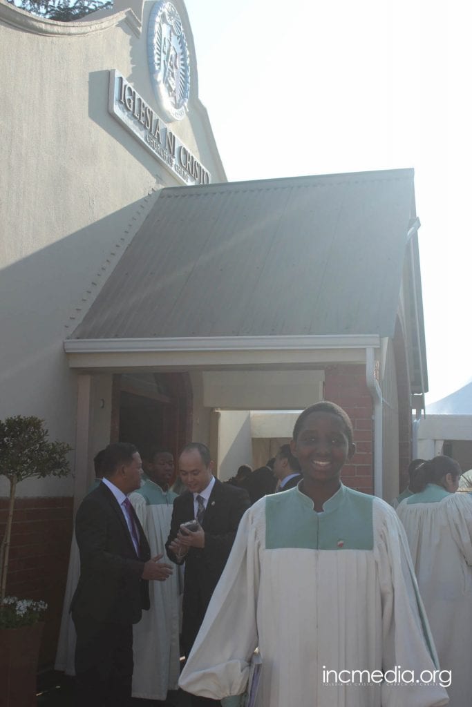 South African person in choir robe in front of worship building.