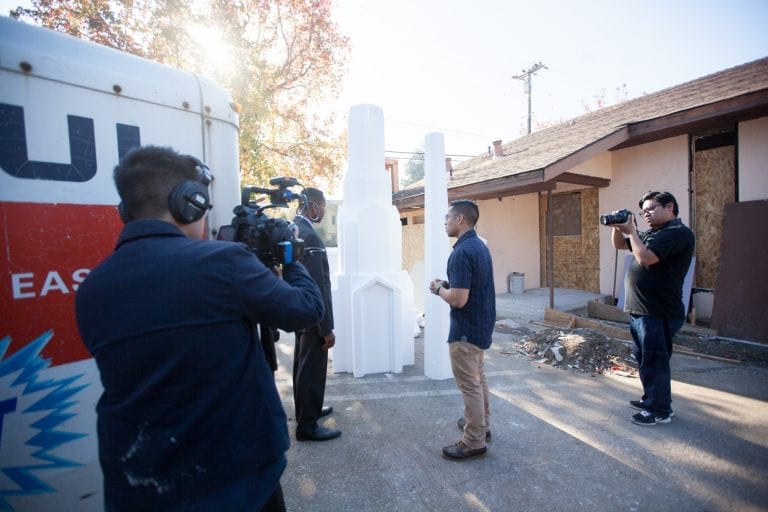 Nan Zapanta interviewing Raymond Frank with 2 camera men besides them next to a few pieces of steeples that will be placed on the roof.