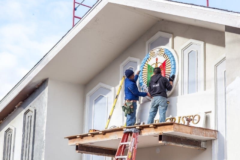 2 construction workers placing the seal of the Church of Christ onto the front facade of the house of worship.