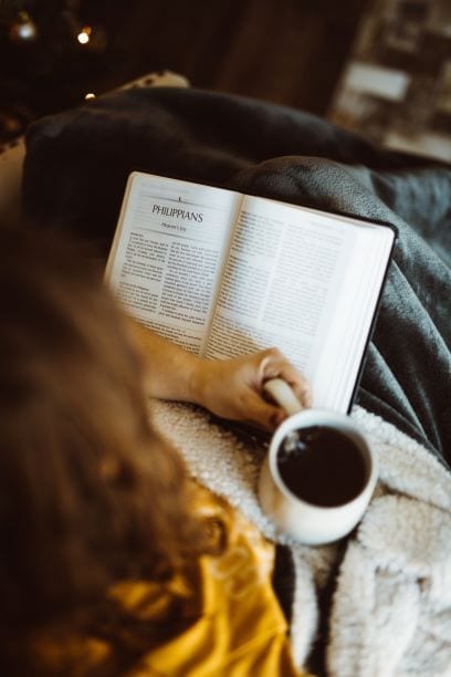 Girl reading Bible with cup of coffee.