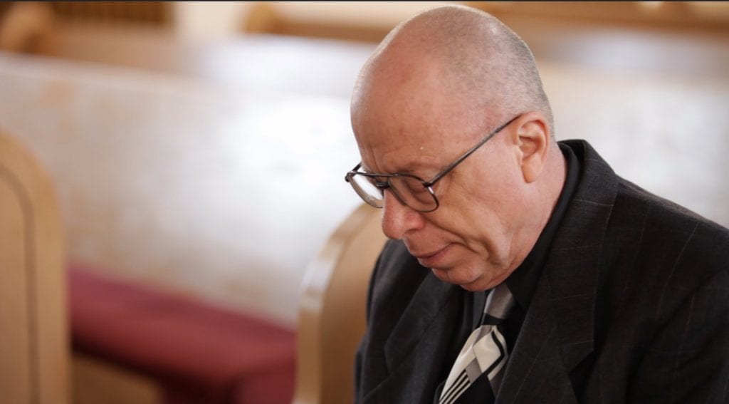 1. Man praying while sitting in the pews of a worship building