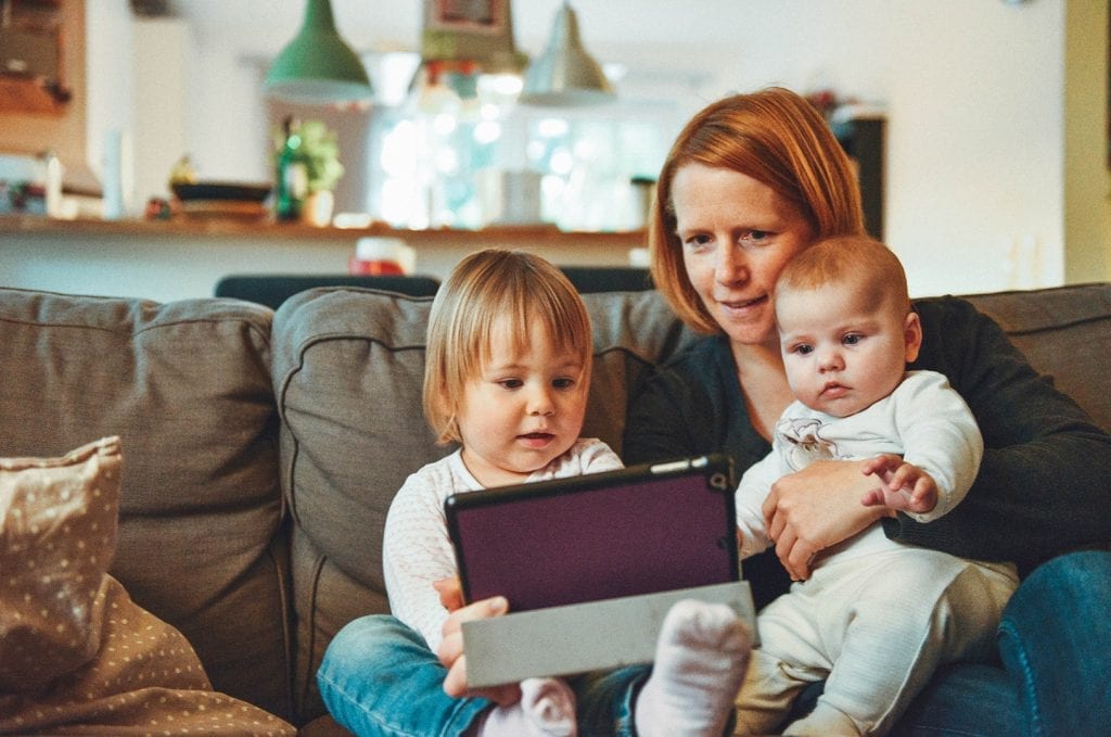 Mom with two kids watching a tablet while sitting
on a couch.