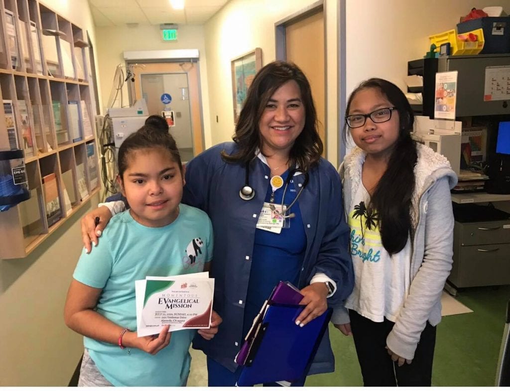 Two girls and a female nurse posing for a photo together smiling.