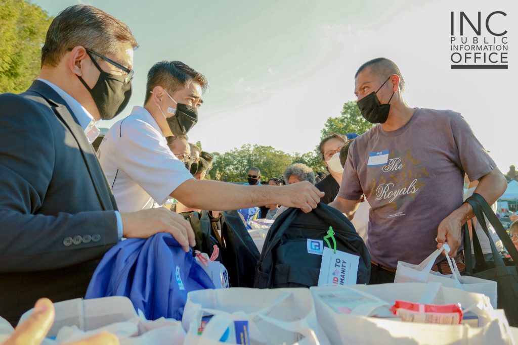 Ministers of the gospel, Brother William Dominguez and Brother Jun Guinto, giving out a book bag filled with school supplies to a parent in attendance