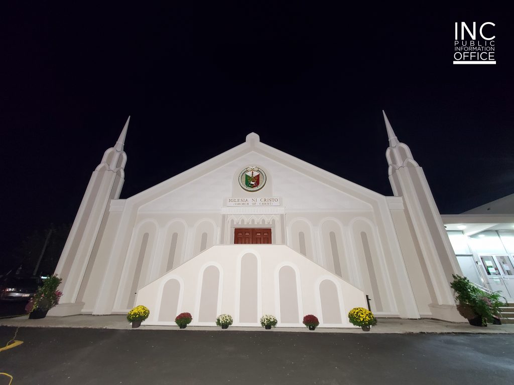 Against the dark night sky, a chapel of the Church Of Christ or Iglesia Ni Criso (INC) with steeples, freshly painted and stuccoed in neutral tones.