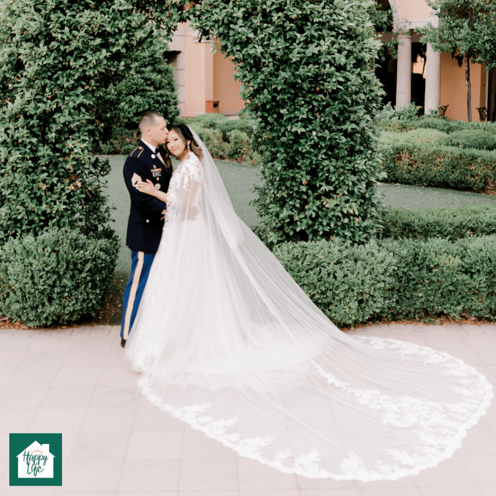 A soldier in military uniform and his new bride pose for a wedding photo in a garden
