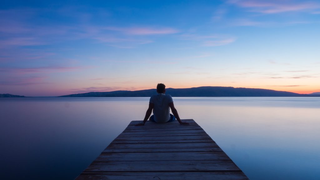 MAN SITTING AT THE EDGE OF A DOCK DURING SUNSET