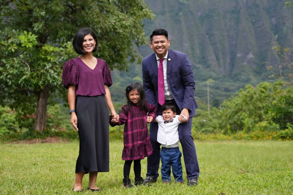 family of four in the grass in front of a tree and grassy hill